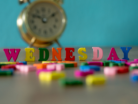 Colorful wooden word WEDNESDAY on wooden table and vintage alarm clock and background is powder blue. English alphabet made of wooden letter color.の写真素材