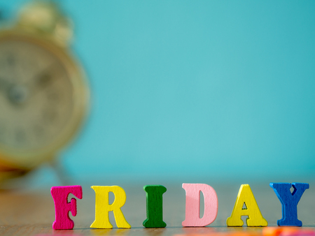 Colorful wooden word FRIDAY on wooden table and vintage alarm clock and background is powder blue. English alphabet made of wooden letter color.の写真素材