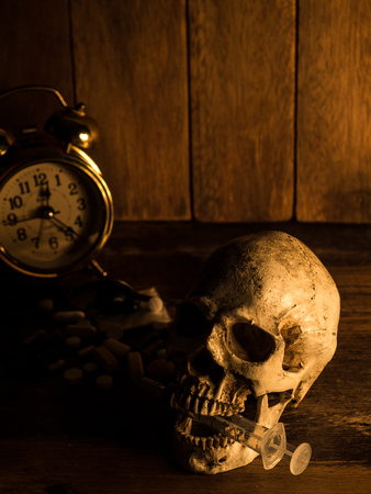 The skull is placed on a wooden table, The back of skull is drug and clock. With candles light from the sides and a wooden background.の写真素材