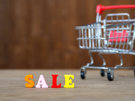 Colorful wooden word SALE on wooden table and shopping cart and background wooden. English alphabet made of wooden letter color. The concept of shopping and Discount festivalの写真素材