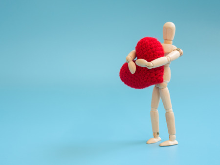 Wooden puppet standing and holding a red heart on the blue screen background. Wooden puppet holding the heart with love and care. Concept of take care and love.の写真素材