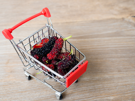 group of mulberries in red shopping cart on wooden table. Mulberry this a fruit and can be eaten in have a red and purple color. Mulberry is delicious and sweet nature.の写真素材