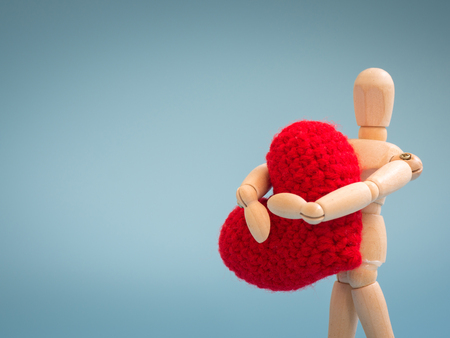Wooden puppet standing and holding a red heart on the blue screen background. Wooden puppet holding the heart with love and care. Concept of take care and love.の写真素材