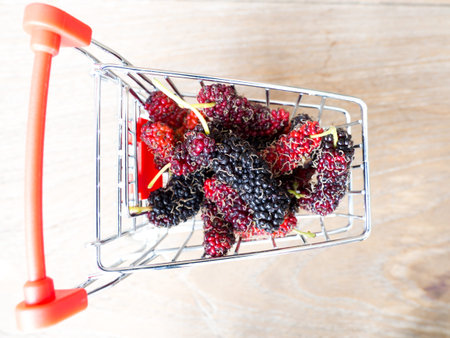 group of mulberries in red shopping cart on wooden table. Mulberry this a fruit and can be eaten in...
