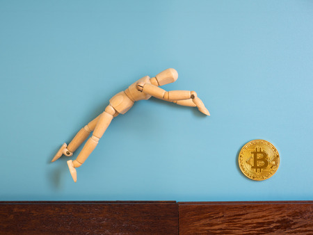 Wooden puppet jumping from the wooden floor in the air to catch the bitcoin.の写真素材
