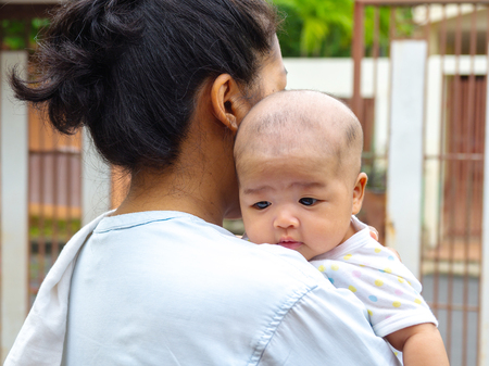 Portrait of happy Asia mother holding his newborn sweet baby dressed. The mommy embracing her baby with love and care. her daughter always happy when she is held.の写真素材