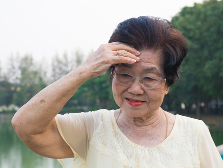 The elderly asian woman wore a glasses. she was not comfortable with headaches.When senior woman walking in the parkの写真素材