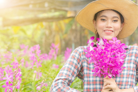 A woman gardener wearing a plaid shirt wearing a hat is holding a pink orchid in his hand. And was smiling happily. In the orchid gardenの写真素材