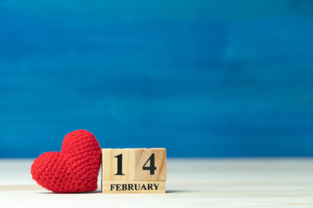 Valentines day concept. hand make yarn red heart beside wooden block calendar set on Valentines date 14 February on wooden table and blue backgroundの写真素材