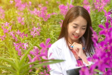 Happy researcher botanical research orchid wearing a white cap and her hand holding a pen and notebook for taking notes for researchの写真素材