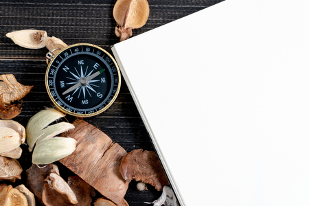 golden compass put on dried leaves and blank notebook on wooden retro black table. Copy space for text and content.の写真素材