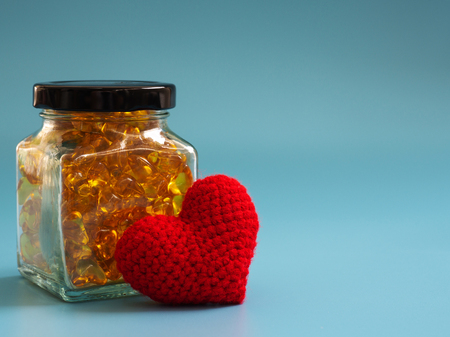Red heart beside Fish oil capsules in glass bottles on blue background. Healthy omega-3 and stethoscope.の写真素材