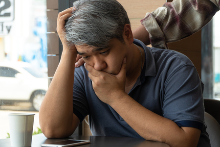 Middle-aged Asian man 40 years old, stressed and tired, are sitting in fast food restaurant and have friends standing behind to encourage. Concept of helping and encouragingの写真素材