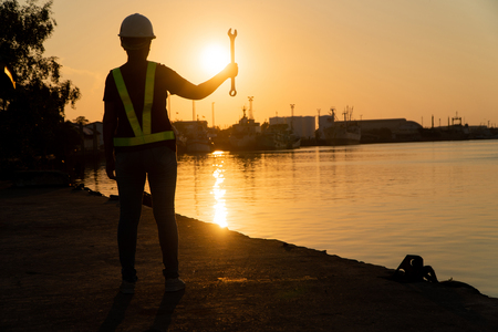 Silhouettes of asian woman engineer holding wrenches and standing on shipyard and background is oil storage silo. Concept of women girl power equal opportunity.の写真素材