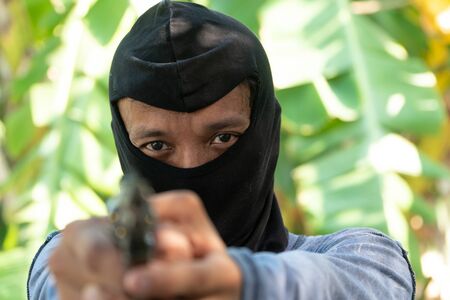Select focus of crime eyes. Robber in black ski mask aims with gunの写真素材