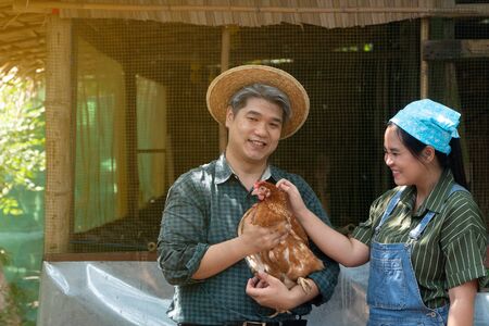 Couples are working at the chicken egg farm. And men are holding hens. Both look happy and healthy.の写真素材