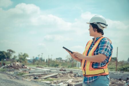 Portrait of Asian woman construction engineer worker with helmet on head using tablet while standing on construction site. building site place on background. Construction conceptの写真素材