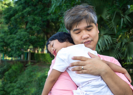 An Asian father is carrying a lovely daughter to her chest and the daughter is lying in the father...