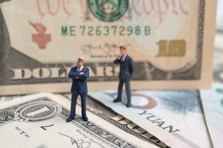 Figure businessman standing on US dollar and YUAN banknote and thinking. Concept of trading warの写真素材