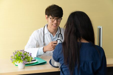 Handsome and young doctor giving a consultation to a patient and Explain medical informations and check blood Pressure in doctor office at hospital. Concept of healthcare and medical serviceの写真素材