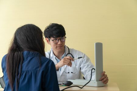 Handsome and young doctor giving a consultation to a patient and Explain medical informations and check blood Pressure in doctor office at hospital. Concept of healthcare and medical serviceの写真素材
