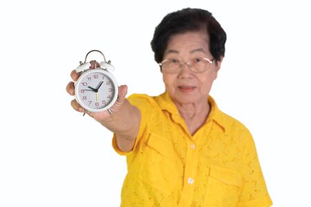 Asian elderly woman holding a white alarm clock on isolated background. The concept aging society That needs time and grandchildren to come back to caring for health careの写真素材