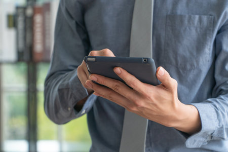 Happy young business man using digital tablet and smiling, standing near the window in office