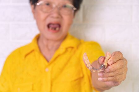 Asian Elderly woman over 70 years old be smile with a few broken teeth and holding dentures in hand. Dentures for prosthetic devices constructed to replace missing teeth and helping to chew food.の写真素材
