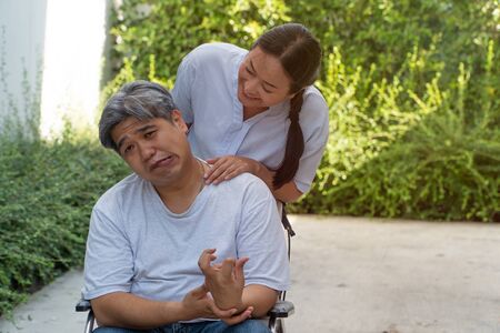 The patient is Cerebrovascular accident or stroke Caused by hypertension and obesity, sitting in wheelchair him mouse is facial palsy, him wife takes care. Concept of healthcare and medical serviceの写真素材