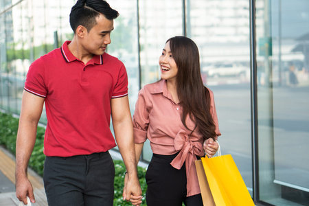 Happy young couple of shoppers walking in the shopping street towards and holding colorful shopping...