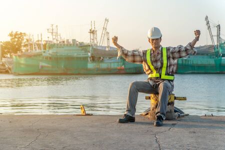 Engineers wearing a safety helmet and sitting. He is raising two hands and feels glad In achieving success. Concept of The concept of determination and determination in the work and achieving successの写真素材
