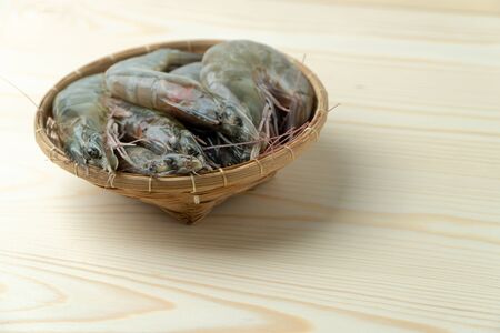 close up group of fresh raw pacific white shrimp in bamboo bowl on wooden table.の写真素材
