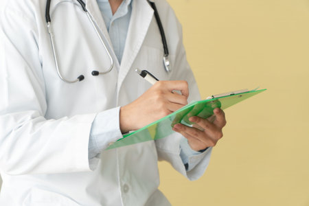 Closeup of asian male doctor writing health report,Medical care or prescription on the green...