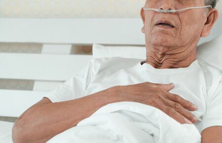 Sad senior man lying on the hospital bed and with a nasal breathing tube for treatment respiratory. Concept of Health care for the elderly, quarantine coronavirus (COVID-19)の写真素材