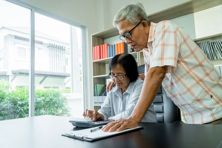 Senior Asian couple using the calculator and paperwork on desk at home to calculate expenses and income. And savings after retirement. Concept of financial planning and investment for retirees.の写真素材