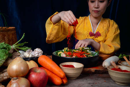 Asian women wearing Korean traditional costumes (hanbok) are mixing fresh stir-fry and kimchi ingredients with ingredients such as salt, garlic, gochugaru, fresh vegetables.の写真素材