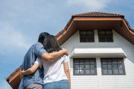 Happy smiling couple in front of the home and holding keys to New Home On Moving In Day, and start a new life family. Concept of homeowner and relocationの写真素材