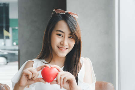 Portrait of beautiful happy Asian woman smiling and holding a red heart. Concept of love and relationship.の写真素材