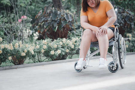 Overweight and obesity woman sitting on wheelchair and holding her knee In pain, cause of Inflammation of his knee to receiving too much weight, Concept of an Overweight problem and Health careの写真素材