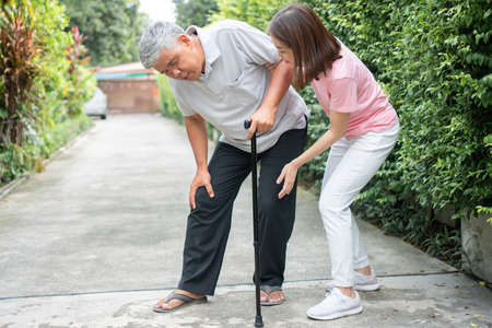 Asian senior man walking in the backyard and painful inflammation and stiffness of the joints (Arthritis) and the daughter came to help support. Concept of old elderly insurance and health careの写真素材