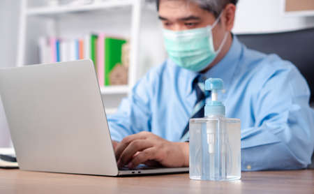 Businessman wearing a mask and have hand sanitizer on his desk for prevention or antibacterial hygiene and Coronavirus disease at the office.の写真素材