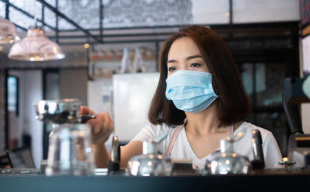 Asian barista women wearing face masks to prevent contagious diseases and serve customers in the coffee shop. The concept of prevention from COVID 19の写真素材