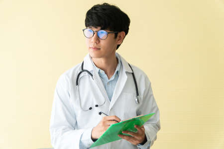 Asian male doctor writing health report, Medical care, or prescription on the green clipboard in hospital. Concept of Medical and healthcare.の写真素材