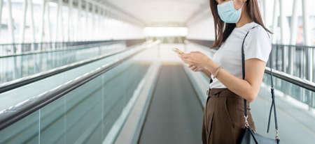 Portrait of a young woman in a medical mask for anti-coronavirus COVID-19 pandemic infectious disease outbreak protection and use a smartphone in Public area. Concept of Virus pandemic and pollutionの写真素材
