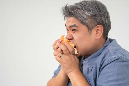 Asian Middle aged man holds and eating a hamburger deliciously Concept of binge eating disorder (BED) and Relaxing with Eating junk food and unhealthy foods.の写真素材