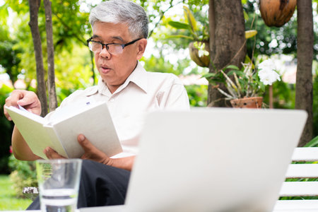senior old man reading a book in the park and drinking water. Concept of retirement lifestyle and...
