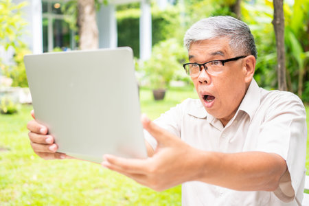 Portrait of an old elderly Asian man is holding a computer laptop and surprised after got some email...