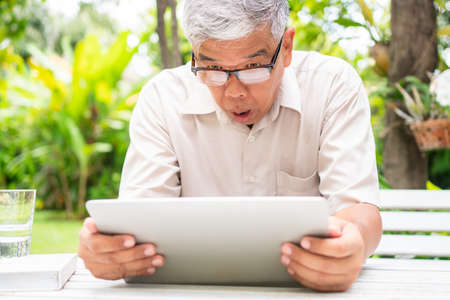 Portrait of an old elderly Asian man is holding a computer laptop and surprised after got some email and read some news in the backyard. Concept of no Ageism and Hobbies after retirement.の写真素材