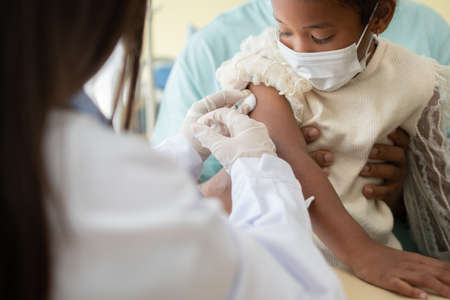 Asian doctor user syringe needle for injection vaccinate,  African American children are being covid vaccinated for prevention coronavirus and flu. Concept of immunization from inoculationの写真素材