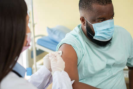Asian doctor user syringe needle for injection vaccinate,  African American is being covid vaccinated for prevention coronavirus and flu. Concept of immunization from inoculationの写真素材